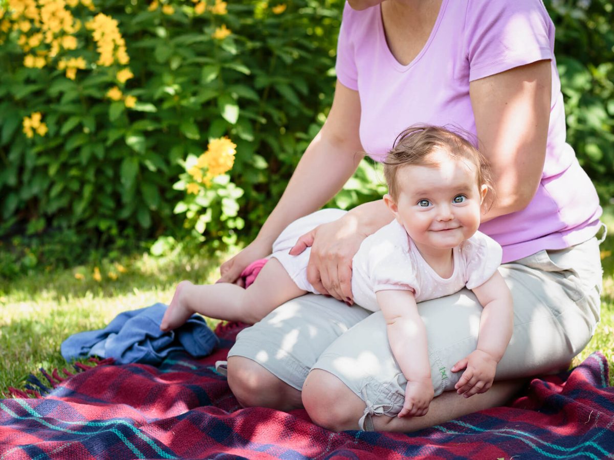 Madre con su bebe en la plaza. El bebe se encuentra acostado boca abajo sobre el regazo de la madre.